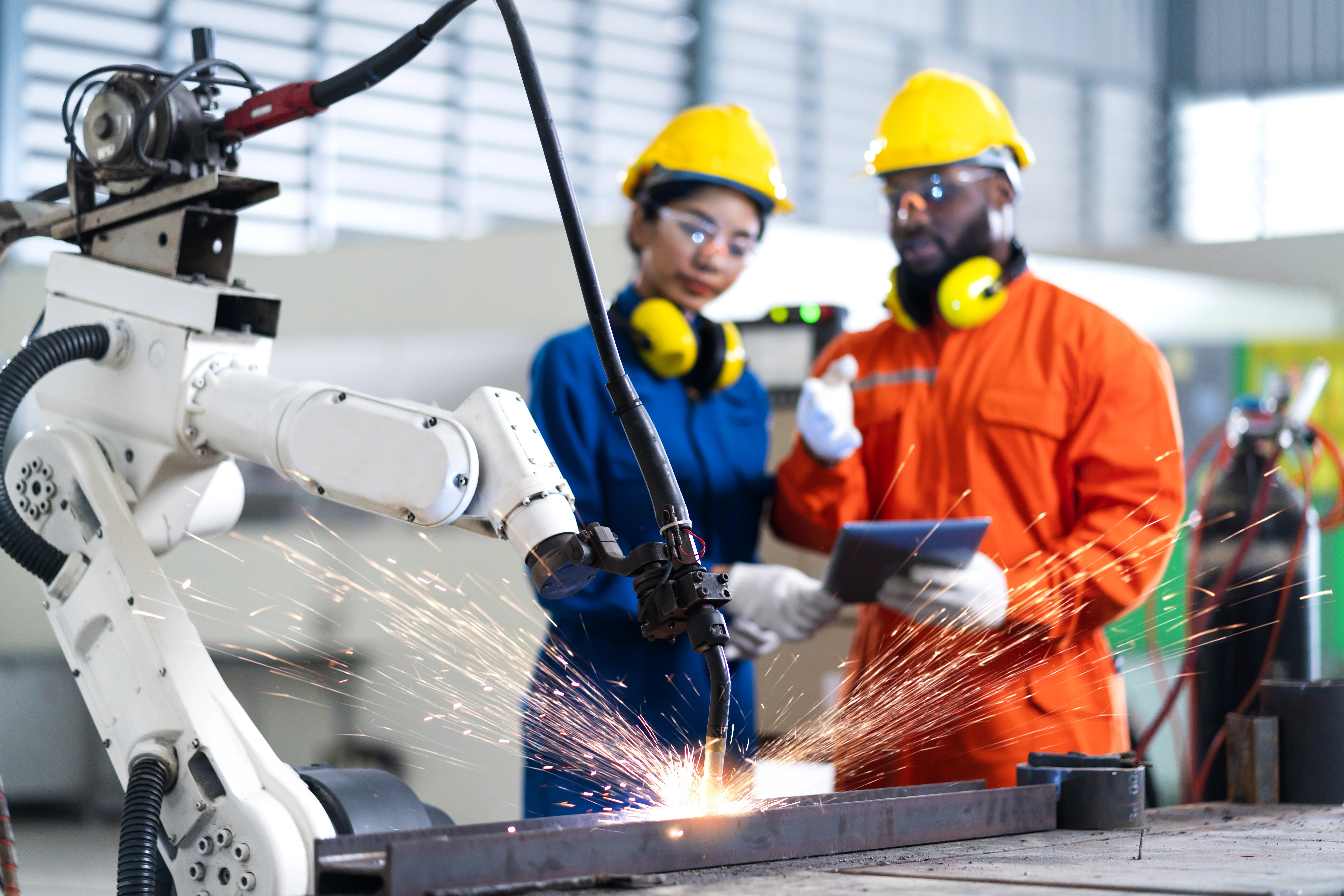 Specialized engineers monitoring a high-precision industrial robotic welding arm in a smart manufacturing facility.