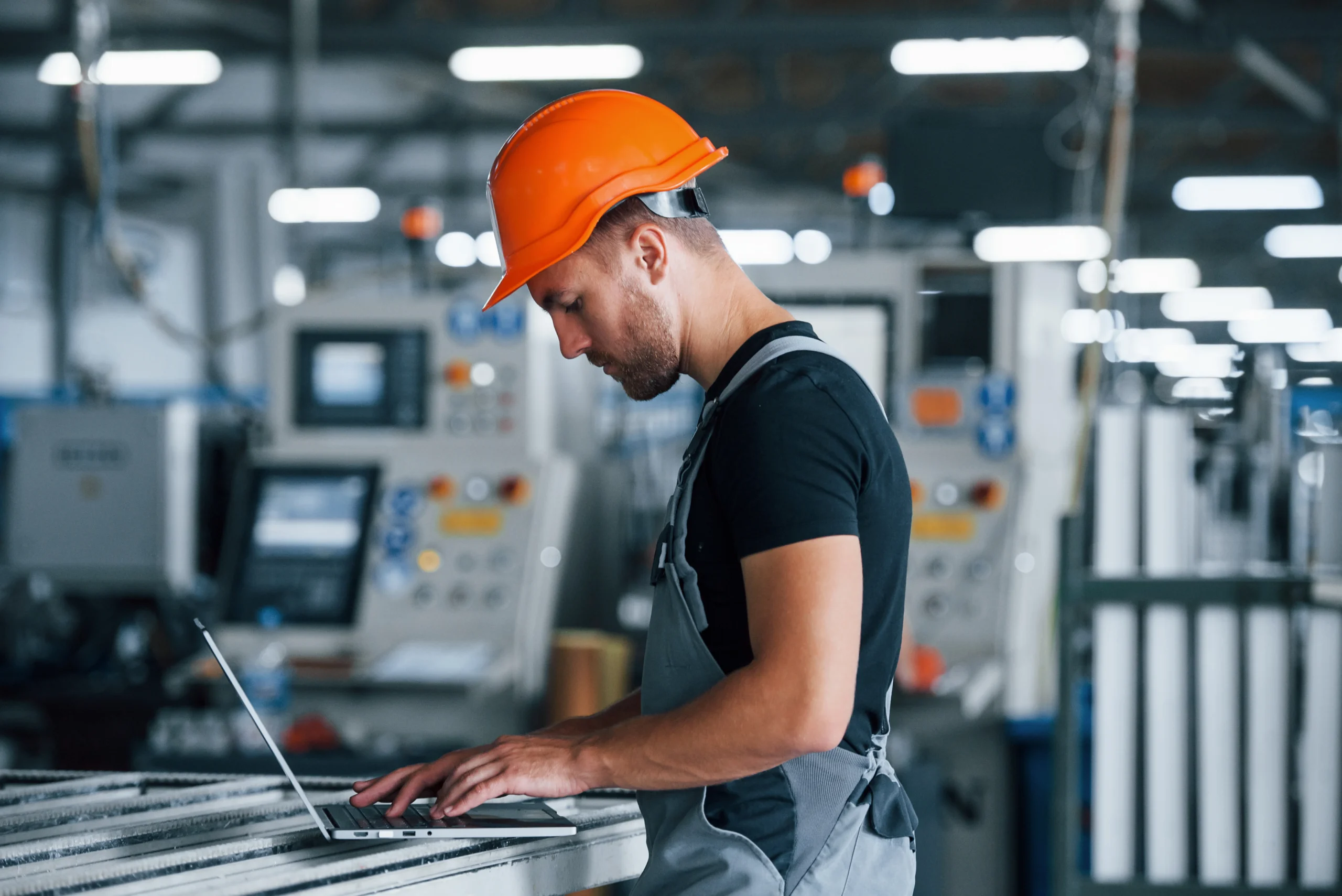 Industrial worker wearing a safety helmet using a laptop inside a manufacturing facility for manufacturing web development and digital operations.